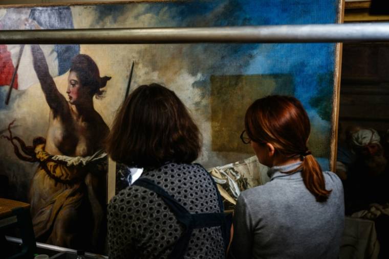 Des restaurateurs travaillent sur le tableau "La liberté guidant le peuple" d'Eugène Delacroix, dans un laboratoire du Musée du Louvre à Paris, le 28 février 2024 ( AFP / Dimitar DILKOFF )