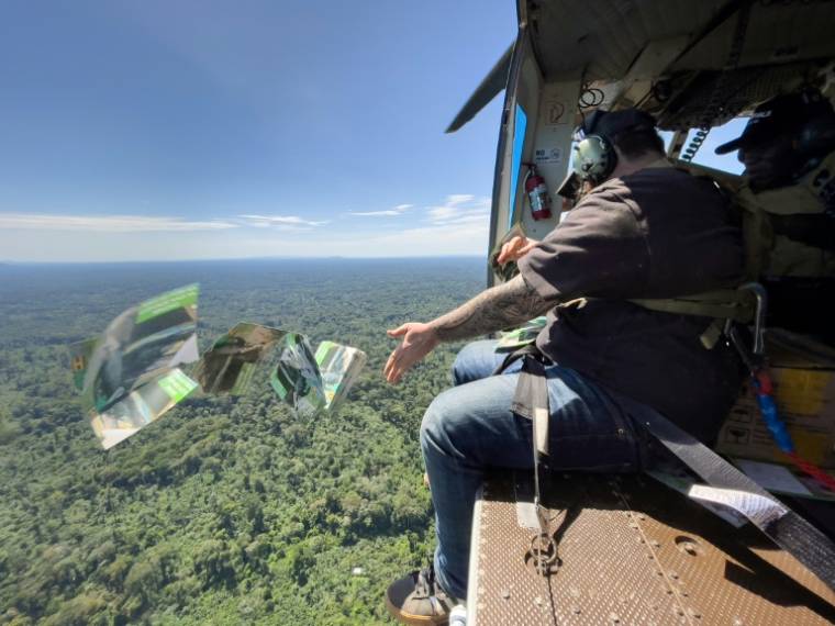 L'Américain Caleb Weiss, employé de la fondation américaine Bridgeway, lance des tracts depuis un hélicoptère sur les bastions des ADF, les exhortant à se rendre, le 8 mai 2024 au-dessus du territoire de Beni, dans la province du Nord-Kivu, dans l'est de la RDC ( AFP / ALEXIS HUGUET )