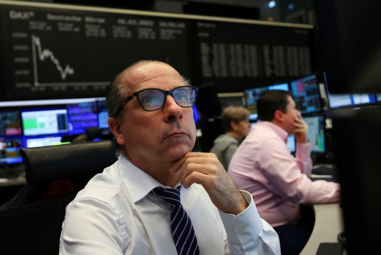 Un courtier en bourse regarde ses écrans devant le graphique de l'indice des prix des actions DAX à la bourse de Francfort