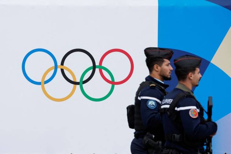 Des gendarmes français passent devant le logo des Jeux Olympiques et Paralympiques de Paris 2024
