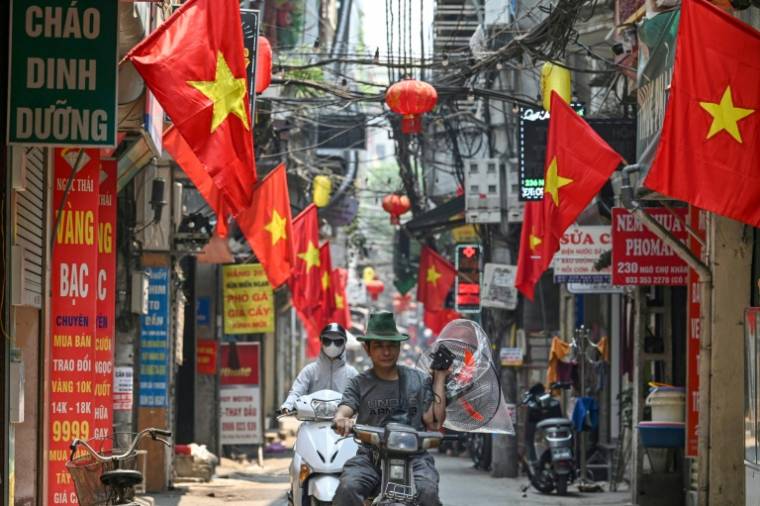 Un homme porte un ventilateur le long d'une rue bordée de drapeaux nationaux vietnamiens à Hanoï, le 30 avril 2024 ( AFP / Nhac NGUYEN )