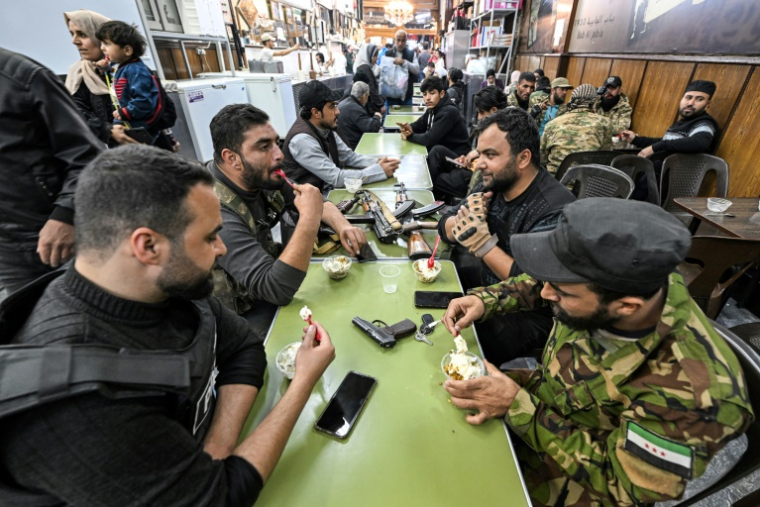 Des combattants de l'opposition syrienne s'assoient pour manger une glace sur le marché d'al-Hamidiya dans la vieille ville de Damas, le 10 décembre 2024 ( AFP / LOUAI BESHARA  )