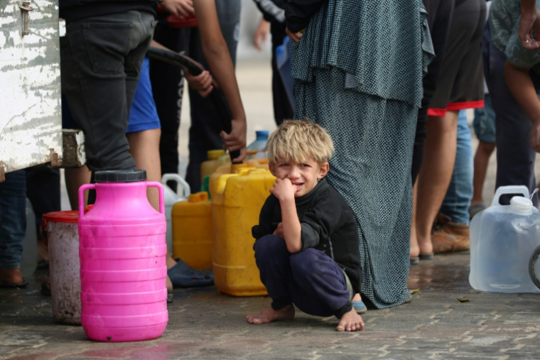 Un enfant palestinien déplacé attend près d'une file de gens qui remplissent des conteneurs d'eau potable, dans le camp de réfugiés d'al-Bureij, dans le centre de la bande de Gaza, le 10 novembre 2024 ( AFP / Eyad BABA )