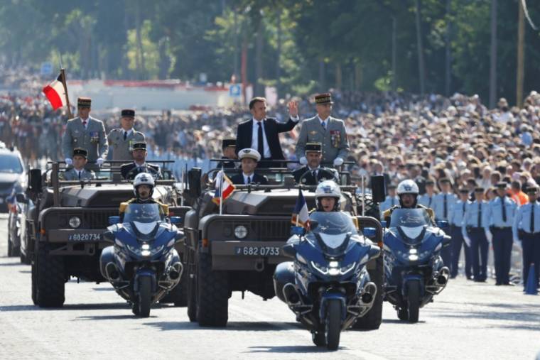 Le président Emmanuel Macron (g) debout dans la voiture de commandement, accompagné du chef d'état-major des armées (CEMA), Thierry Burkhard (d), lors du défilé militaire sur l'avenue Foch,le 14 juillet 2024 à Paris ( AFP / Ludovic MARIN )