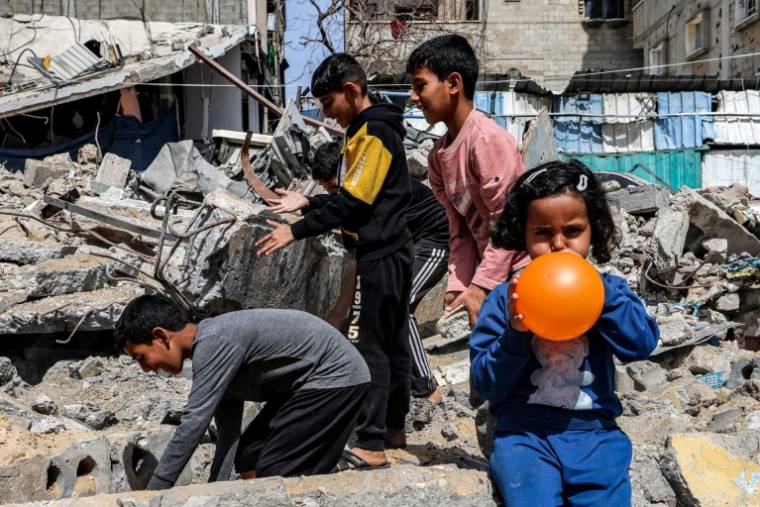 Une petite fille gonfle un ballon pendant que des garçons fouillent les décombres d'un bâtiment détruit à Rafah, dans le sud de Gaza, le 5 avril 2024 ( AFP / MOHAMMED ABED )