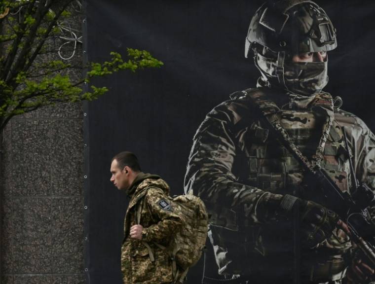 Un soldat ukrainien passe devant une affiche de recrutement pour l'armée, à Kiev le 23 avril 2024 ( AFP / Sergei SUPINSKY )