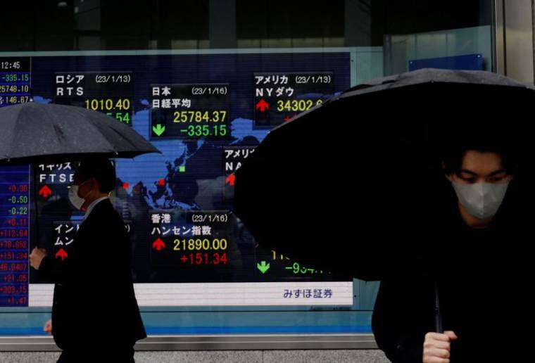 Des hommes passent devant un tableau électrique affichant les indices Nikkei et d'autres pays devant une maison de courtage à Tokyo