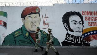 Des miliciens passent devant une fresque murale figurant l'ancien président vénézuélien Hugo Chavez et le libérateur Simon Bolivar, le 7 janvier 2025 à Caracas ( AFP / Pedro MATTEY )