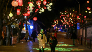 Des piétons dans une rue décorée de lanternes  à la veille de la nouvelle année lunaire du serpent à Pékin, le 28 janvier 2025 ( AFP / GREG BAKER )