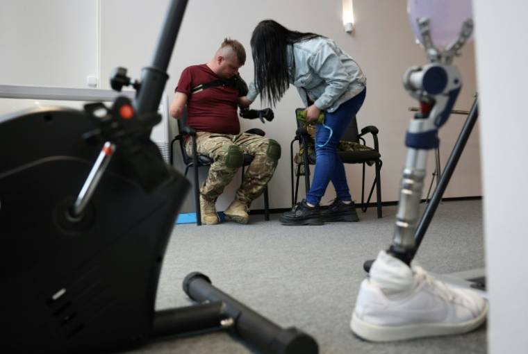 Veronika Koutcherenko aide son mari Valeriï à positionner sa prothèse bionique dans les locaux de l'ONG américaine Protez Foundation, le 2 avril 2024 à Kiev ( AFP / Anatolii STEPANOV )