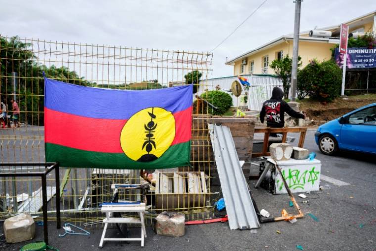 Un drapeau kanak sur un barrage dans le quartier de Magenta, à Nouméa, où un manifestant régule la circulation, le 22 mai 2024 en Nouvelle-Calédonie ( AFP / Theo Rouby )