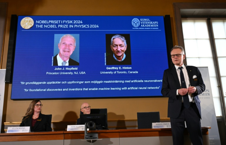 Les deux lauréats du prix Nobel de physique, le Britanno-canadien Geoffrey Hinton et l'Américain John Hopfield, apparaissent sur un écran au moment où le membre du comité Nobel Anders Irbaeck (d) prononce un discours après l'annonce de leur récompense à Stockholm, le 8 octobre 2024 ( AFP / Jonathan NACKSTRAND )