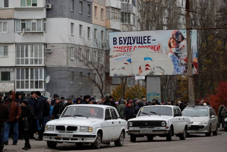 Des personnes attendent la distribution d'aide humanitaire, avec un panneau publicitaire pro-russe en arrière-plan, à Kherson
