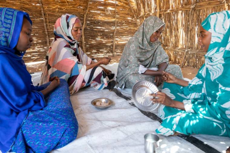 Des réfugiés soudanais partagent un bol d'une bouillie à base de sorgho dans un abri à l'intérieur du camp d'Adre, au Tchad le 10 avril 2024 ( AFP / Joris Bolomey )