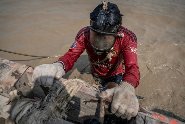Un homme plonge dans les eaux boueuses du fleuve Yangon pour remonter des épaves, le 27 février 2024 à Rangoun, en Birmanie ( AFP / Sai Aung MAIN )