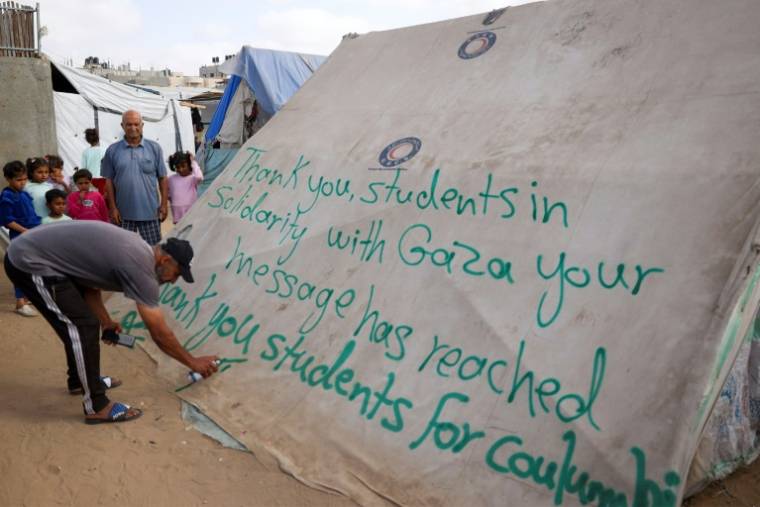 Un homme écrit un message de remerciement aux étudiants américains sur une tente dans un camp de déplacés palestiniens à Rafah, dans le sud de la bande de Gaza, le 27 avril 2024 ( AFP / - )