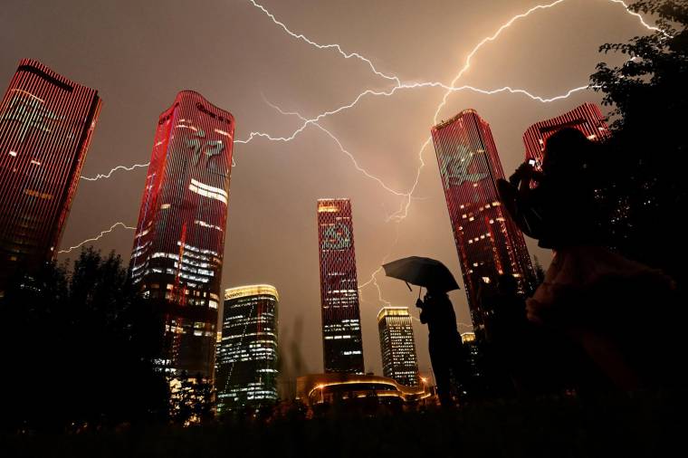 Un éclair traverse le ciel alors que les gens regardent des bâtiments affichant un show lumineux à la veille du 100e anniversaire du Parti communiste chinois à Pékin le 30 juin 2021. ( AFP / NOEL CELIS )