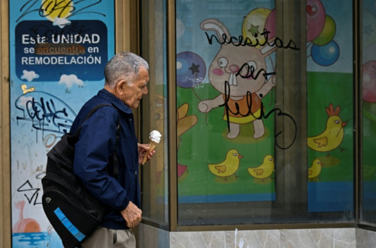 Un homme marche devant le graffiti "Necesitas ser feliz" (Tu dois être heureux) du graffeur cubain Mr. Sad, à La Havane, le 12 décembre 2024 ( AFP / YAMIL LAGE )