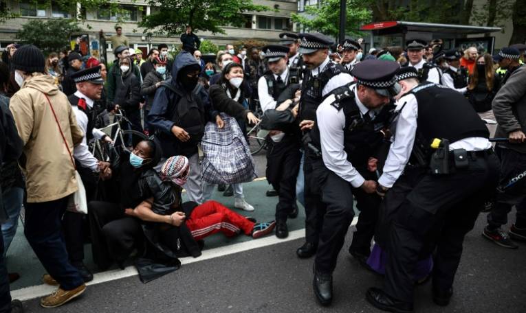 Des policiers arrêtent des manifestants rassemblés autour d'un bus en attente de transporter des migrants et des demandeurs d'asile d'un hôtel de Peckham, au sud de Londres, vers la barge Bibby Stockholm à Portland, dans le Dorset, au sud-ouest de l'Angleterre, le 2 mai 2024 ( AFP / HENRY NICHOLLS )