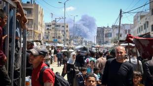 Des Palestiniens marchent dans une rue le 7 mai 2024 alors que de la fumée s'élève dans le ciel après une frappe israélienne à Rafah, dans le sud de la bande de Gaza, où une guerre oppose Israël au mouvement islamiste palestinien Hamas ( AFP / - )