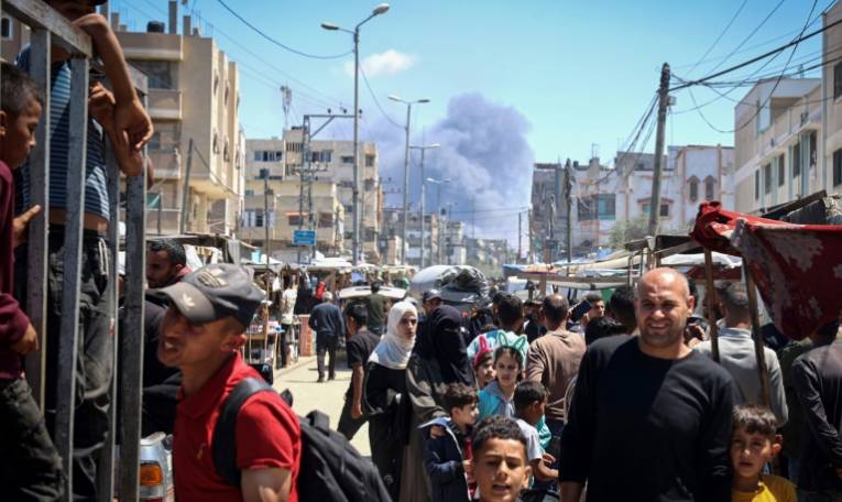 Des Palestiniens marchent dans une rue le 7 mai 2024 alors que de la fumée s'élève dans le ciel après une frappe israélienne à Rafah, dans le sud de la bande de Gaza, où une guerre oppose Israël au mouvement islamiste palestinien Hamas ( AFP / - )