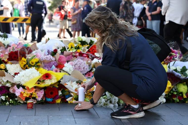 Une femme allume une bougie après avoir déposé des fleurs, le 14 avril 2024, en hommage aux victimes de l'attaque au couteau dans un centre commercial à Sydney ( AFP / DAVID GRAY )