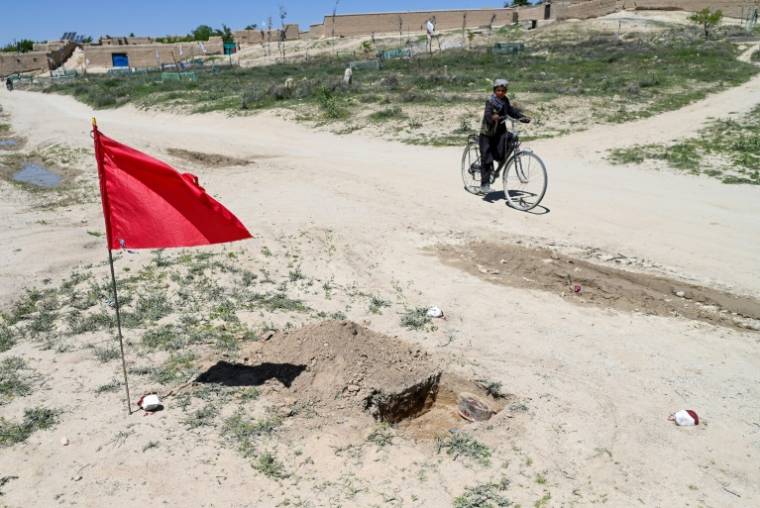 Un enfant à vélo passe près d'une mine antichar non explosée signalée par un drapeau rouge près du village de Qach Qala, dans la province de Ghazni, le 14 mai 2024 ( AFP / Wakil KOHSAR )