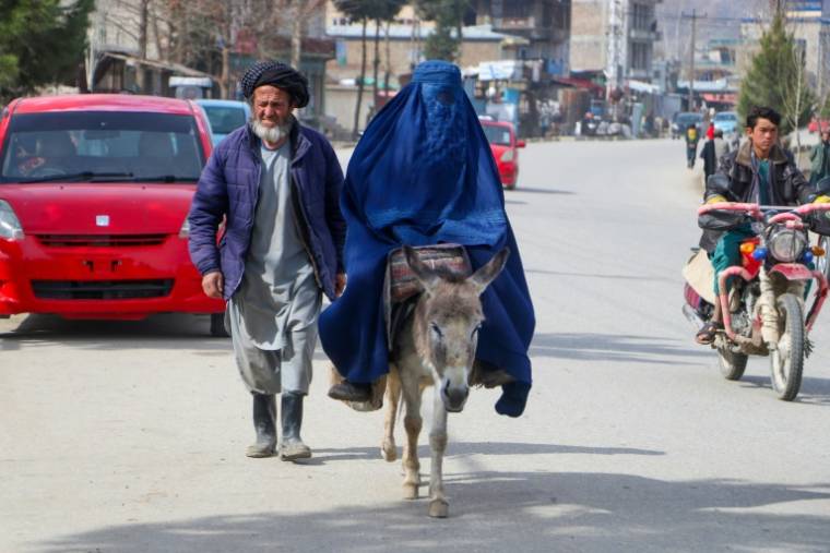 Une femme en burqa, se déplace à dos d'âne, accompagnée d'un homme à Fayzabad, le 14 mars 2024 en Afghanistan  ( AFP / OMER ABRAR )